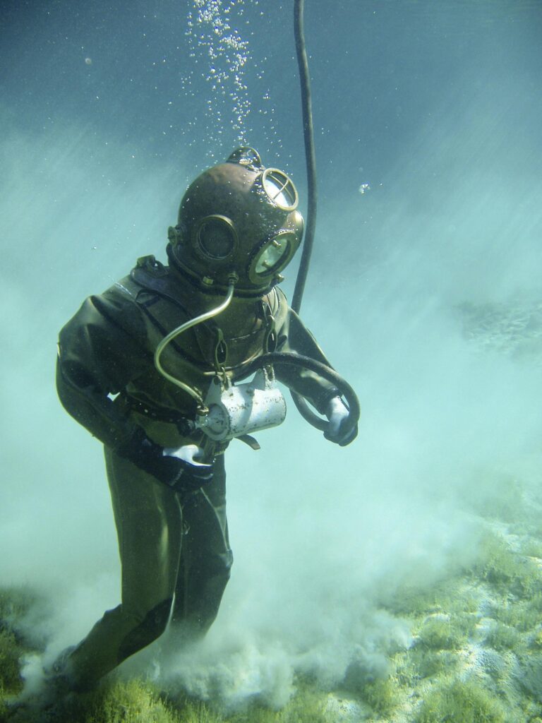 A vintage diver in a classic suit explores underwater, surrounded by clouds of sand.